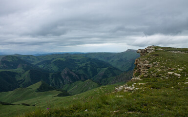 Fototapeta premium Panoramic view of green mountains and hills from the Bermamyt plateau in Karachay-Cherkessia in Russia on a cloudy summer day and copy space in a hazy haze on the horizon