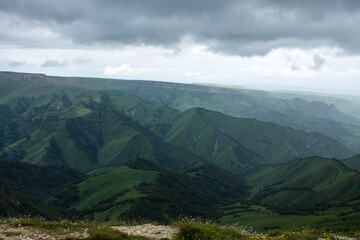 Fototapeta premium Panoramic view of green mountains and hills from the Bermamyt plateau in Karachay-Cherkessia in Russia on a cloudy summer day and copy space in a hazy haze on the horizon