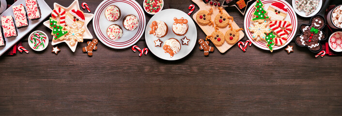 Cute Christmas sweets and cookie top border. Above view on a rustic dark wood banner background with copy space. Fun holiday baking concept. - Powered by Adobe