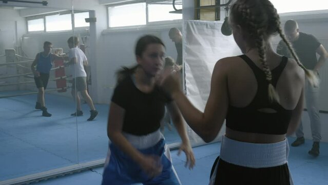 Teen girls sparring at boxing class, children group practicing kicks in gym, handheld shot. Boxer training kids in combat sport club, boys and girls workout