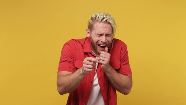 Young excited cheerful fun blond man with dreadlocks 20s he wear red shirt white t-shirt look camera laugh smiling watch comedy movie pointing index finger on you isolated on plain yellow background