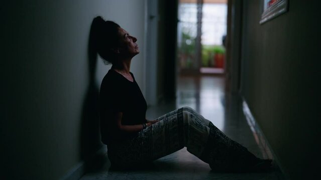 Middle age hispanic woman suffering for domestic violence with bruise on eyes sitting on floor at home