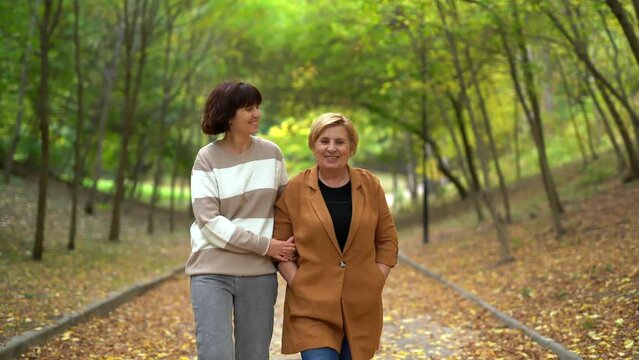 Mother's day concept. Portrait of senior pensioner mom and adult cheerful daughter together outdoor in park in falling season. Mother and daughter walking in autumn park. High quality 4k video