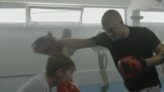 Boxing coach training kid, teacher and child sparring, children class workout, teenagers group practicing kicks in gym. Boy exercising in combat sport club