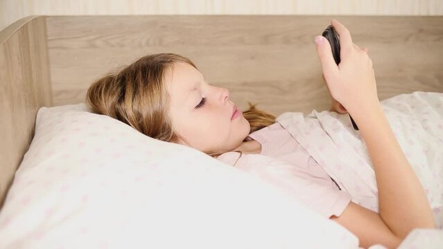 child lying in bed playing mobile phone.