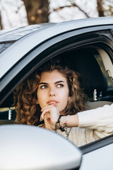 Fototapeta na wymiar young curly girl in a white sweater against the backdrop of autumn nature and her own car