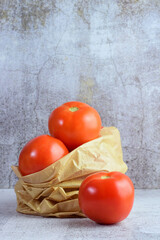Round red tomato in a paper bag on a stone background.