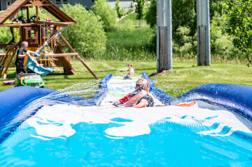 Selective focus on child going down a water slide with water spraying.