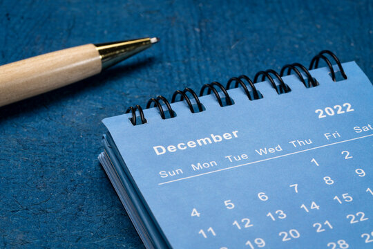 December 2022 - spiral desktop calendar against blue textured paper with a stylish pen, low angle shot, time and business concept