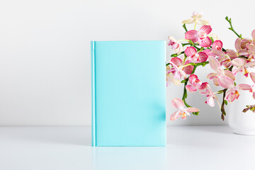 Blue book mockup, bouquet flower pink orchids in glass vase. Front view. Place for text, copy...