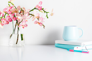 Home Office, notepad, pen, cup, bouquet flower, pink orchids in glass vase. Front view. Place for text, copy space, mockup