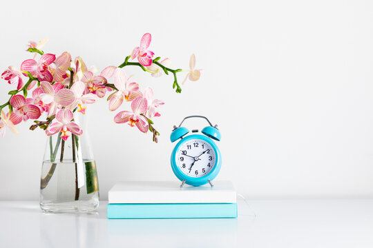 Switching to summer or winter time, alarm clock, notepad, bouquet flower, pink orchids in glass vase. Home Office. Front view. Place for text, copy space, mockup