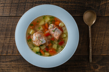Fresh salmon fish soup with carrots, potatoes and red peppers in a white plate, close up. Tasty dinner consists of a fish soup with salmon. Top view