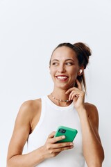 Naklejka premium Young millennial woman listening to music on wireless headphones through her phone and smiling at home on a white background