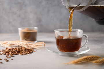 Pouring barley coffee in glass cup on gray background. Cooking healthy caffeine free alternative...
