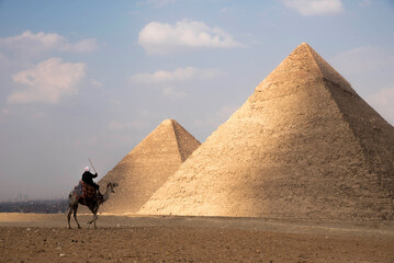 A man riding a camel at Great Pyramids of Giza, Cairo, Egypt - obrazy, fototapety, plakaty