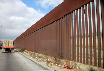 View of border wall with as seen driving on road with truck in the distance