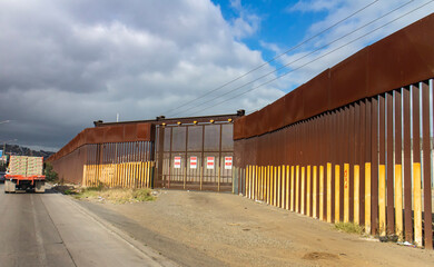 View of border wall with as seen driving on road with truck in the distance