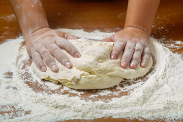 The hands of a Jewish woman knead the dough for challah for a festive meal on a wooden table.