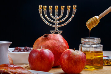 challah, wine, apples and honey dripping honey from a spoon into a jar.
