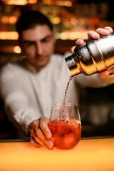 close-up view on shaker in male hand from which cocktail is poured into glass