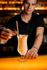 close-up view of glass of cocktail that the hands of bartender decorate with green leaves