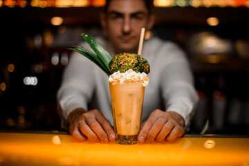 close-up of glass with signature cocktail garnished with whipped cream and pineapple
