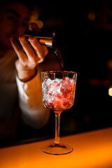 selective focus on crystal glass in which bartender pours alcoholic drink from jigger