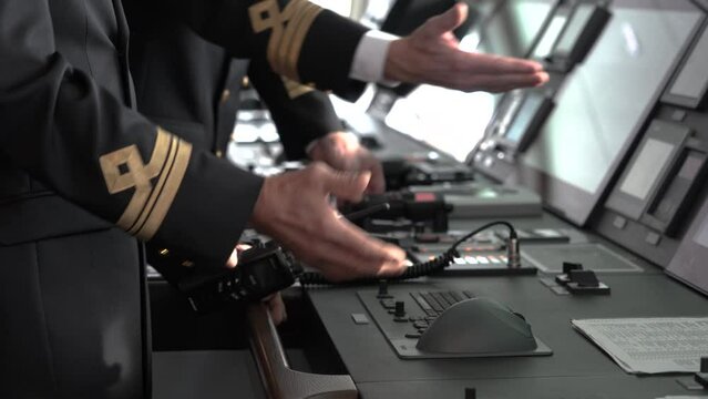 Ship's bridge. Officers show to screens of control panel. Hand holding radio. hief Mate, second mate patches on jackets.