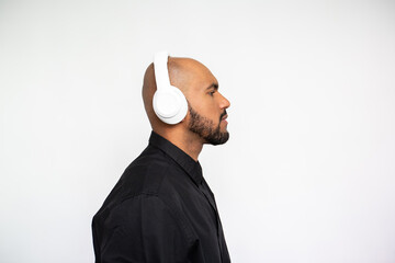 Side view of serious young man in headphones posing against white background. Bearded businessman wearing black shirt standing and looking away. Music and leisure concept - Powered by Adobe
