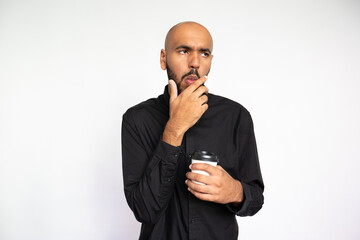 Portrait of impressed young man with coffee. Thoughtful African American male model with bald head in black shirt looking away, touching chin. Coffee break, approval concept