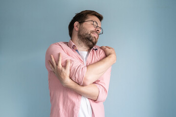 Man embraces himself, dreamily closing eyes. Blue background.