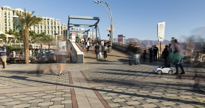 Time lapse of people walking at eilat boardwalk in front of the red sea, the hotels cityscape and moab mountains at the background, Eilat, Israel