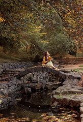 a girl sits on a bridge with dried leaves in her hands in the park. High quality photo