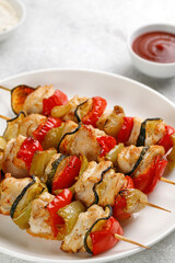 Roasted Chicken kebab meat with vegetables, sweet pepper, zucchini on skewers on white plate and grey background. Dinner diet concept.