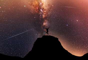 Hiker silhouette jumping on the hill, behind them fantastic beautiful night sky with milky way...
