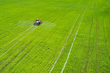 Obraz na płótnie Canvas Protection of agricultural seedlings from pests and diseases. A self-propelled sprayer sprays pesticides on a green field. Shooting from a drone.