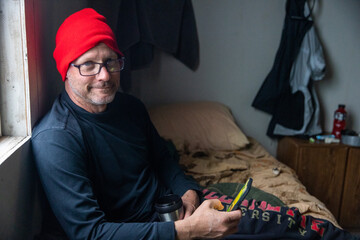 Friendly man with a nice smile wearing a red hat while holding his phone and a coffee cup in a rustic cabin