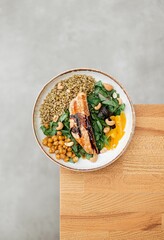 Vertical shot of a salmon dish in a white plate on the corner of a wooden table