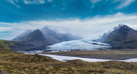 Glacier tongue slides from the Vatnajokull icecap or Vatna Glacier near subglacial Oraefajokull volcano, Iceland. Glacial lagoon with ice blocks and surrounding mountains.