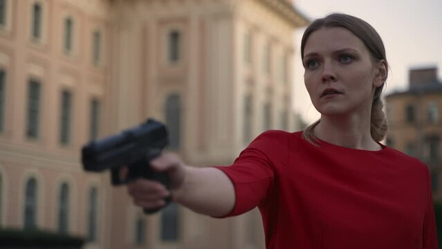 4k Young woman is holding gun and standing on street of old city spbd. Closeup view of beautiful European female holds gun and looks with confused emotion, poses for camera and stands in town on