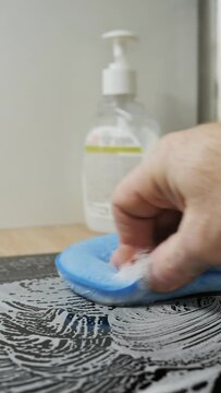 Cleaning the ceramic hob from burnt fat with a blue soft sponge and a cleaning agent in a bottle with a manual dispenser. vertical video. Dolly shot, closeup