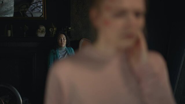 4k Young woman aims at another female and stands in dark room spbd. Killing eve concept. Beautiful female killer is holding weapon in hand and aiming at frightened person, showing confusion for camera