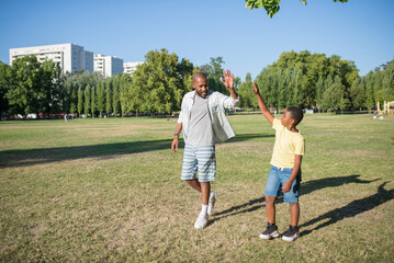 Portrait of smiling African man and boy walking on field. Bearded dad and his son in casual clothes...