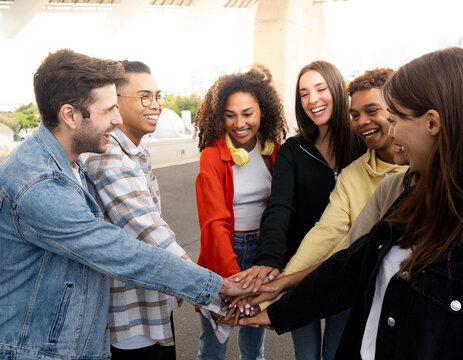 Group of multi-ethnic young friends stacking hands celebrating. Young millennials having a good time