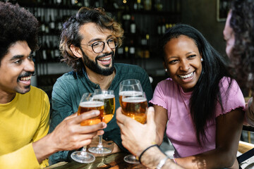 Group of diverse friends enjoying weekend together cheering with beers at brewery bar - International friendship concept