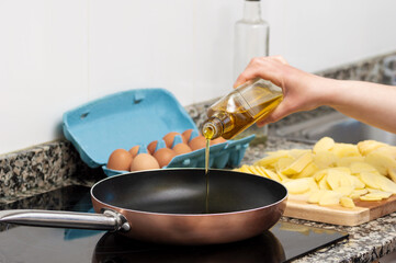 Cropped shot of a woman pouring cooking oil from bottle into frying pan on stove