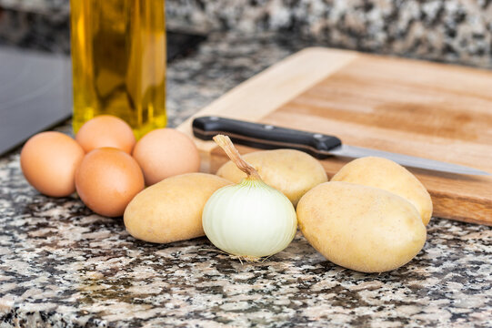 Potatoes, oil and onion in a kitchen with a wooden board on top of a marble table .Concept of preparing an traditional spanish omelette