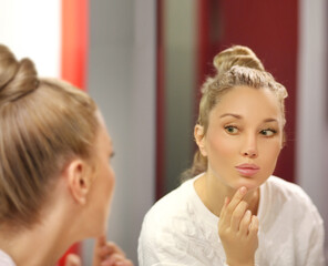 Fototapeta premium woman looking in the mirror in the bathroom and taking care of her skin.Applying the cream..Magic anti-aging cream.
