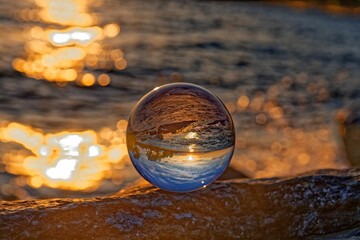 Glass ball reflecting sunny sky with bokeh shiny water in the background